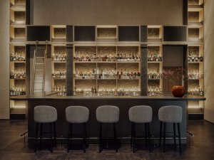Aman Rosa Alpina Bar – elegante Hotelbar mit beleuchteter Regalwand und Barhockern | nova-reisen