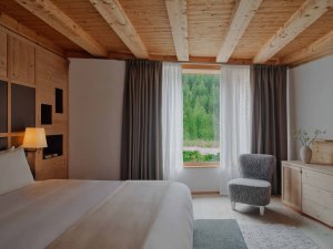 Aman Rosa Alpina Zeno Suite – Schlafzimmer mit Fensterfront, Vorhängen und Sessel | nova-reisen