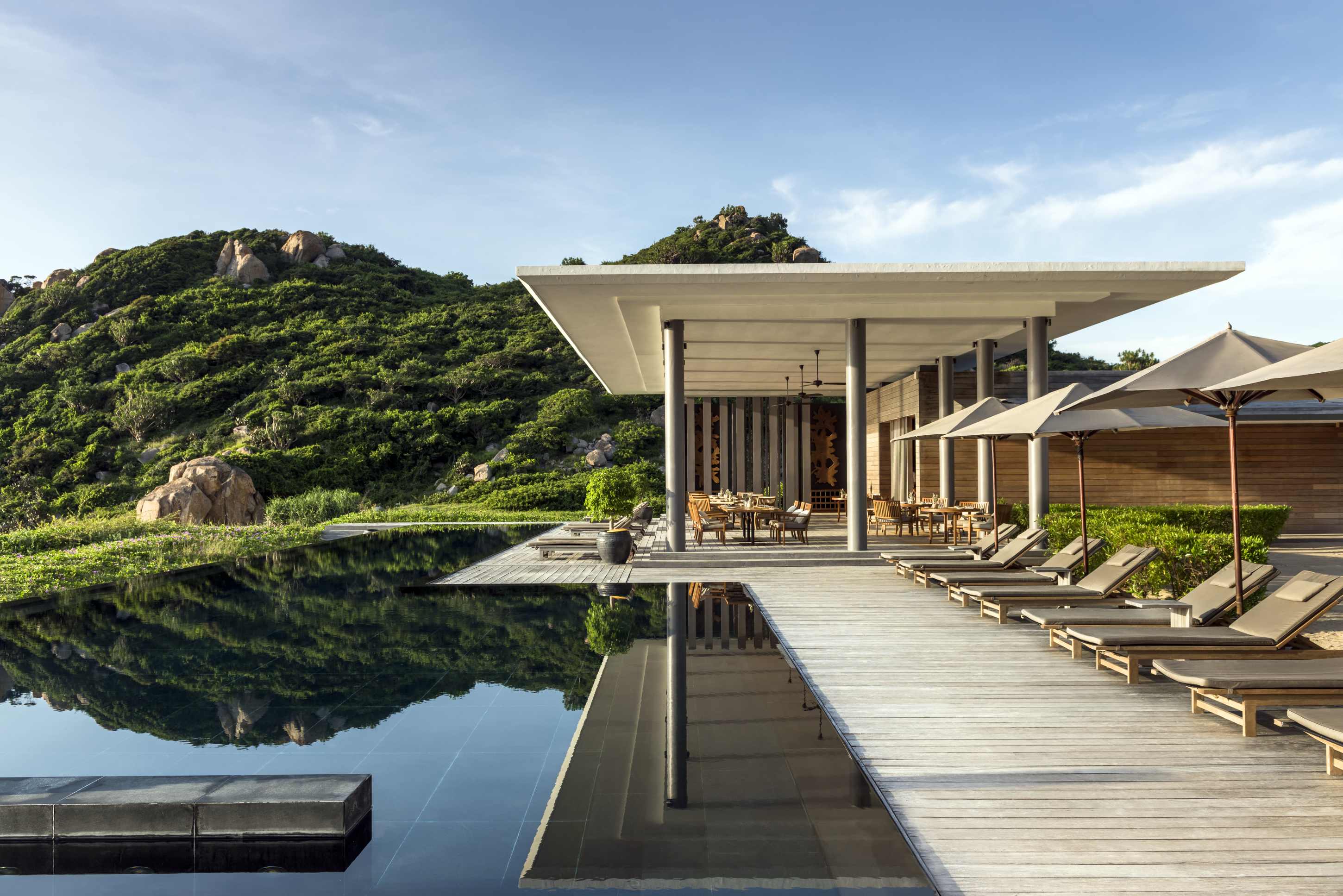 Amanoi Vietnam Beach Club – Poolterrasse am Wasser mit Daybeds, moderner Architektur und Blick auf die Bucht | nova-reisen