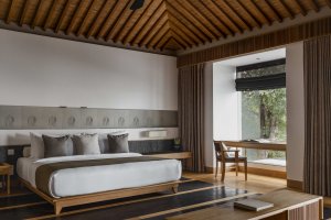 Amanoi Vietnam Living Pavilion – offener Wohnbereich mit Sofa, Holzdecke und angrenzendem Schlafzimmer im Resort-Design | nova-reisen