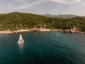 Amanoi Vietnam Catamaran – Luftaufnahme eines Katamarans vor der Küste mit türkisblauem Wasser und grünen Hügeln | nova-reisen