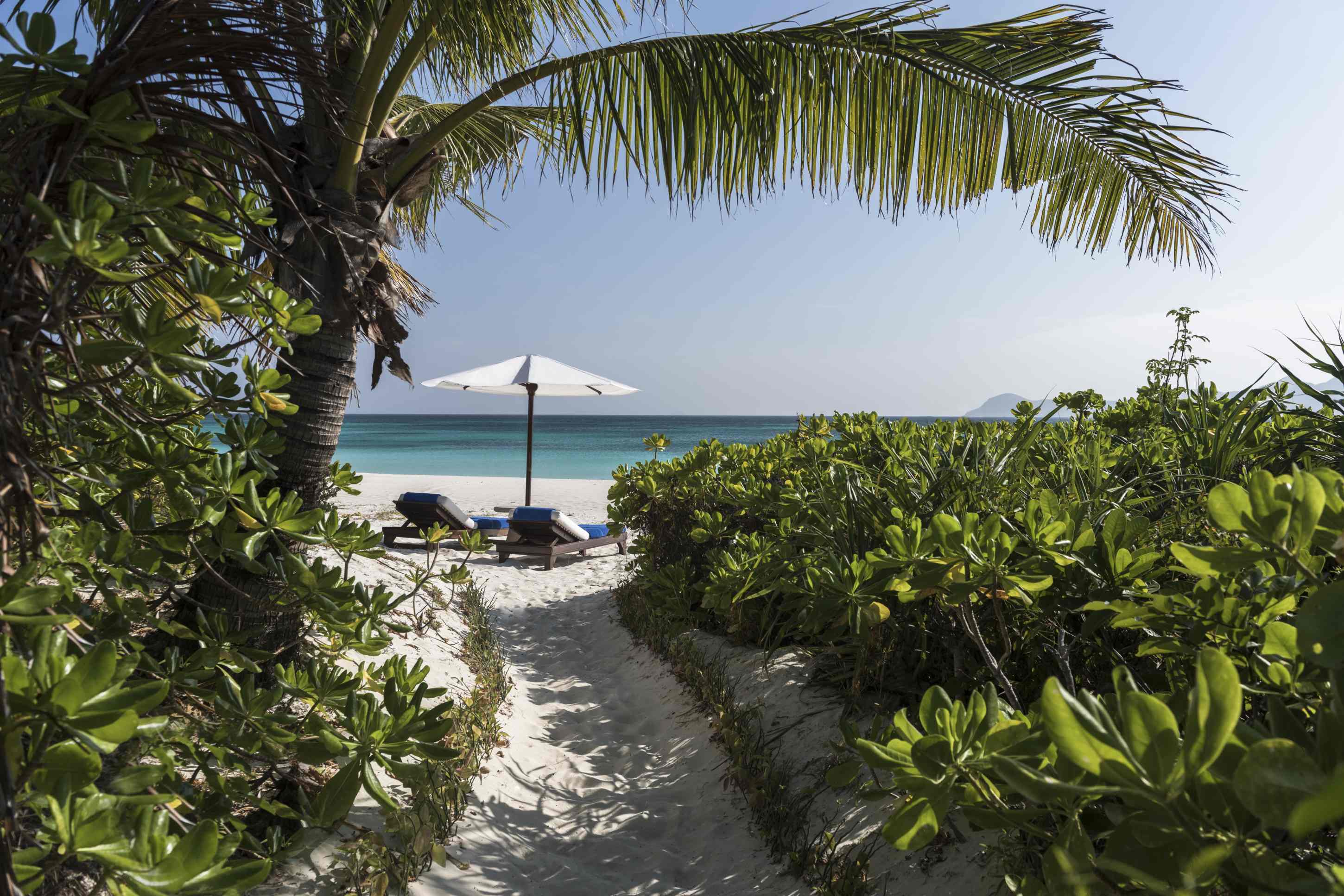 Amanpulo Philippinen Beach Casita – schmaler Pfad durch Palmen und Garten zur Strandbucht | nova-reisen