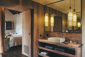 verblasstes retro foto von einem badezimmer mit waschbecken aus einem stein und viel holz ein grosser spiegel ist da und davor hängen asiatische lampen es gibt handtücher und viele pflegeprodukte im schönen exklusiven klassischen urigen und altmodischen h