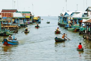 foto von einem schwimmenden dorf die häuser schwimmen auf holz plateaus mit auto reifen aussen dran in der mitte eine wasser strasse mit vielen kanus und kleinen booten darauf die menschen darauf beim schönen exklusiven klassischen urigen und altmodischen