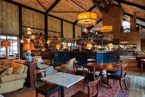 klassisches restaurant im country style mit marmor und holztischen und sofa und grosser bar mit vielen gläsern und alkohol flaschen und hoher holzdecke im exklusiven soho farmhouse in england Oxfordshire