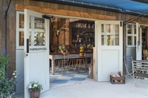 klassischer bauern laden farm shop im ländlichen stil mit viel holz einem hirschgeweih und davor eine terasse mit blumen tisch und brennholz im exklusiven soho farmhouse in england Oxfordshire