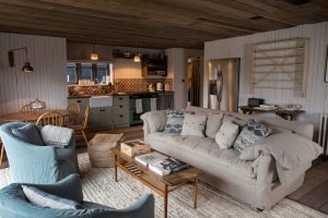 klassisch eingerichtetes wohnzimmer mit einer grossen couch und gemütlichen sesseln und einem sehr grossen kühlschrank dazu einbe schöne küche und das alles im altmodischen ländlichen country stil im exklusiven soho farmhouse in england Oxfordshire