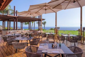 sonnige terrasse mit gedeckten tischen und blick in den garten und auf das meer im luxushotel the ritz carlton abama auf teneriffa mit schattenspendenden sonnenschirmen unter blauen himmel