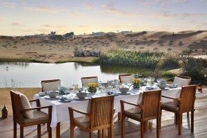 gedeckter esstisch an einem kleinen see im orientalischen edlen luxus designer hotel the ritz carlton ras al khaimah in der al wadi wüste in den vereinigten arabischen emiraten im orient mit schafen im hintergrund auf den dünen